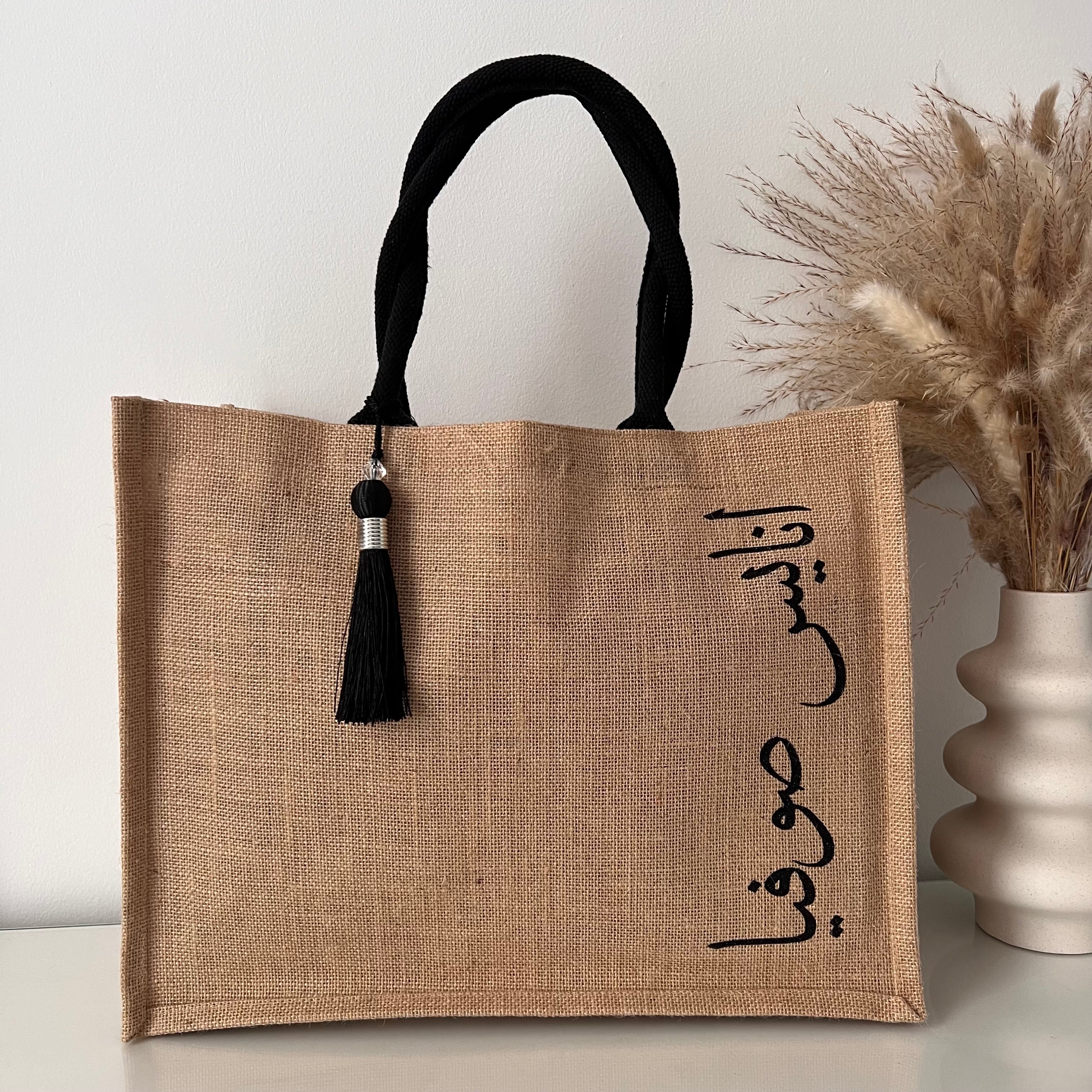 Sac en Toile de Jute avec Pompon Noir et Personnalisé avec Prénom en Calligraphie Arabe sur le coter